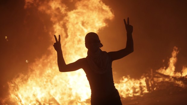 An anti-government protester makes victory signs in front a fire set by protesters to block a road during a demonstration in Beirut, Lebanon.