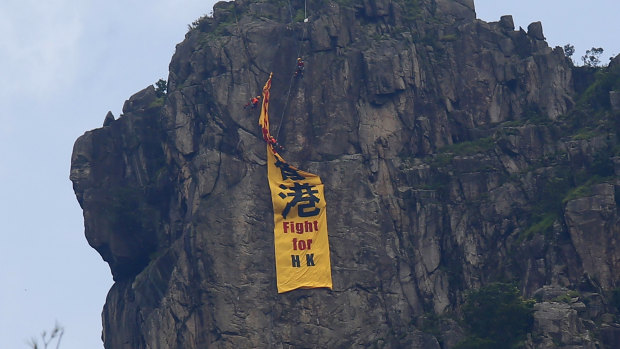 Firefighters remove a yellow banner with the words "Fight for Hong Kong" in Chinese and English on the Lion Rock mountain by pro-democracy protesters in Hong Kong.