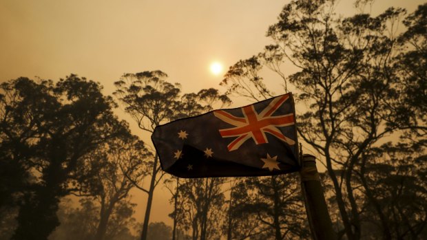 The Australian flag flies on a property as smoke from a bushfire approaches.