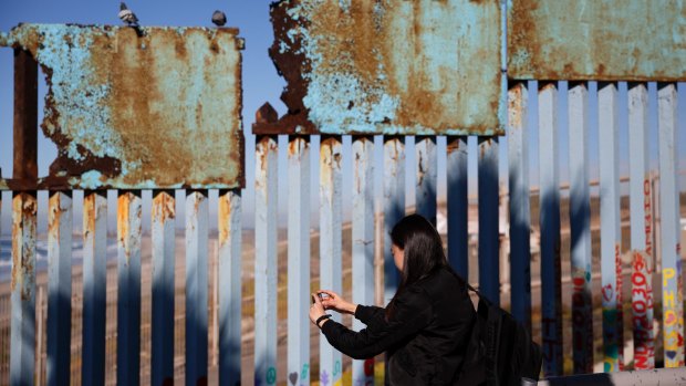 A woman takes pictures as birds sit along a rusted top section of the current US-Mexico border wall near the beach in Tijuana, Mexico.