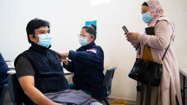 Sri Indreswari photographs her husband, Arbi Yanno, receiving his COVID-19 vaccination at the All Saints Grammar School gymnasium in Belmore. 