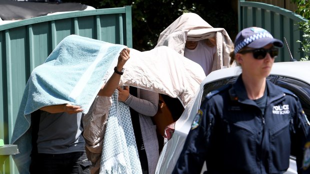 People covered in sheets and towels are escorted from a house during the NSW Police raid.