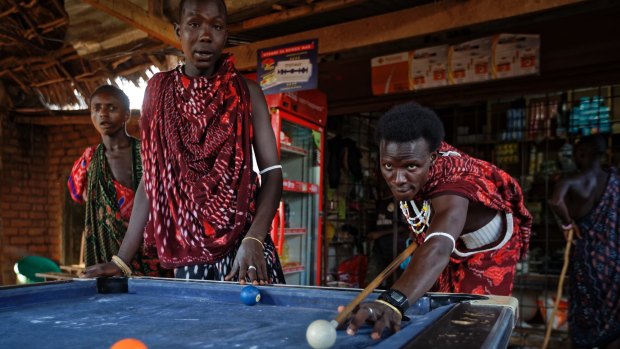 Young Maasai men relax and play a game of pool at a bar by the side of the road in the late afternoon at Mkata junction, near Mikumi National Park.