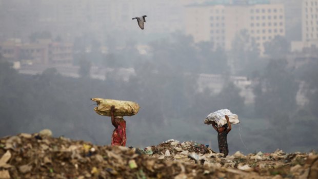 A young Indian ragpicker follows her mother as they carry reusable garbage at a dumping ground on the outskirts of New Delhi, India.