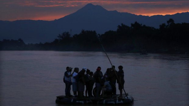 Central American migrants stand on a raft to cross the Suchiate River from Guatemala to Mexico, with the Tacana volcano in the background, near Ciudad Hidalgo, Mexico.