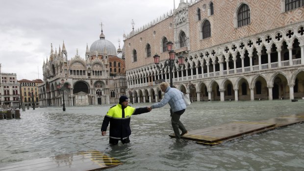 A city worker helps a woman who decided to cross St. Mark square on a gangway, in flooded Venice last month.