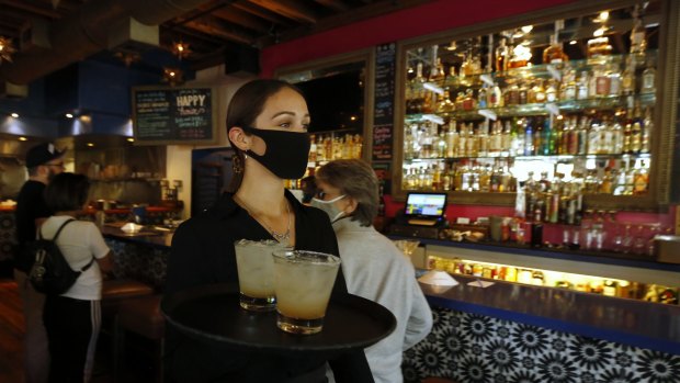 A masked waitress serves drinks in a bar in California. 