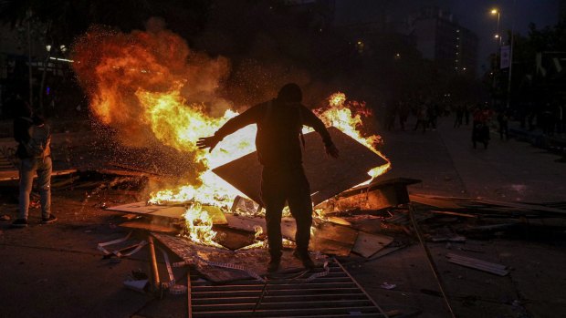 A wet anti-government protester dries his clothes by standing close to a burning street barricade in Santiago, Chile. 
