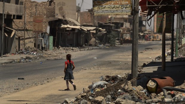 A girl walks across a street surrounded by debris and destroyed buildings in West Mosul after fleeing Islamic State in June 2017.