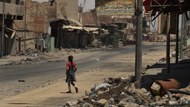 A girl walks across a street surrounded by debris and destroyed buildings in West Mosul after fleeing Islamic State in June 2017.