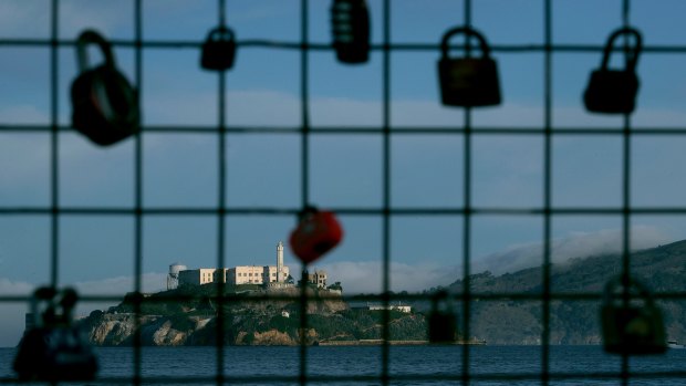 Alcatraz Island is shown behind a locks on a pier fence in San Francisco. Some tours to the island have stopped because the ferry is government-run.