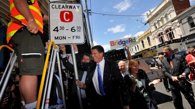 Then-Premier Ted Baillieu replaces the old clearway sign with a new sign to restore the original clearway times after winning the 2010 election. Traders pop open the champagne.