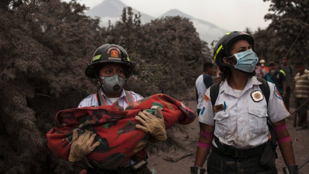 A firefighter carries the body of a child recovered near the Volcan de Fuego, in Escuintla, Guatemala.