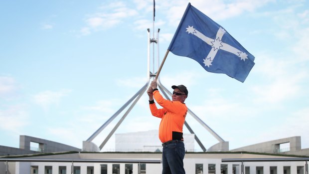 A CFMMEU representative flies the Eureka flag in front of Parliament House.
