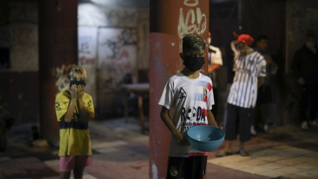 A child in a protective face mask and holding a container waits to be served at a soup kitchen on the outskirts of Buenos Aires. 