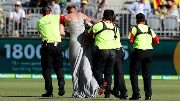 The streaker is escorted off the ground by security during the stadium's first-ever sports fixture.