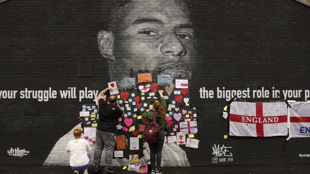 People place messages of support on a defaced mural of Marcus Rashford in his hometown. 