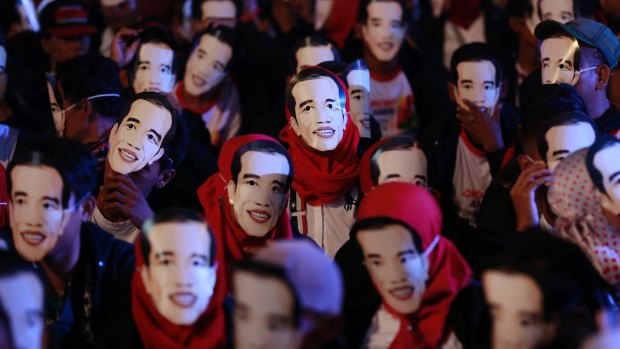 People wear masks depicting Indonesian President Joko Widodo during a rally.