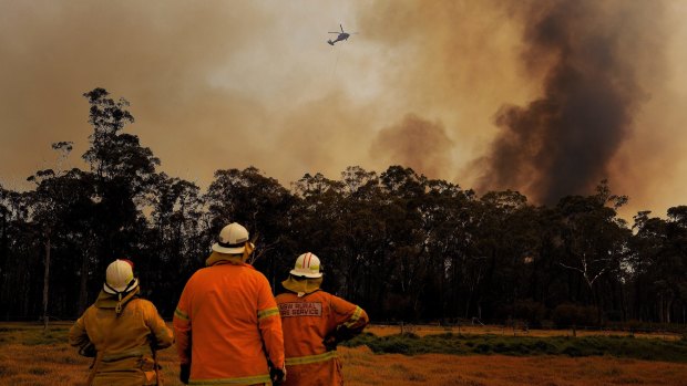 NSW RFS firefighters monitor a fire as a helicopter dumps water overhead at Tahmoor.