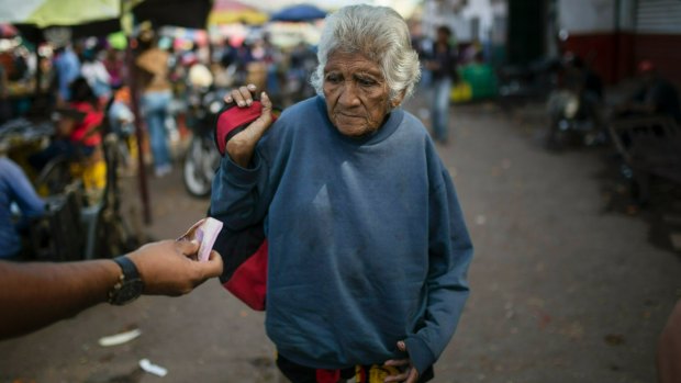 An elderly woman is offered cash as she begs at a wholesale food market in Caracas. 