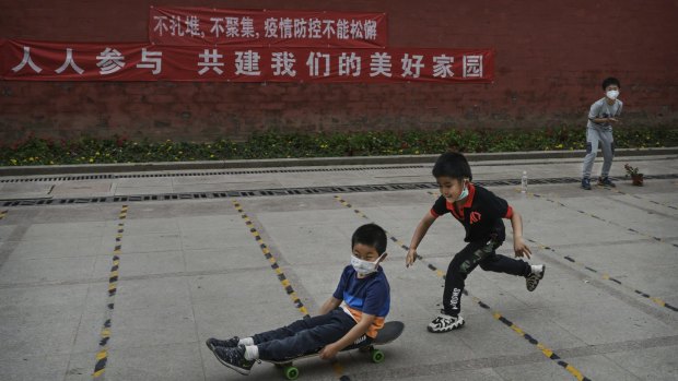 A young Chinese boy pushes a friend who wears a protective masks as he rides on his skateboard while they play at a small park in Beijing.