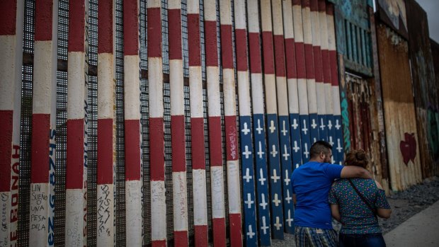 Pedestrians pass in front of a section of a US-Mexico border wall in Tijuana.