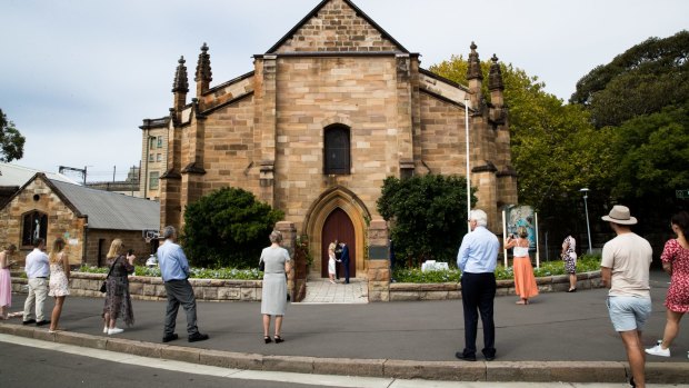 Bystanders, who were not invited to the wedding, practice social distancing on the street while Brigette Leech and Matthew Selby are married by Minister Justin Moffatt, at the Garrison Church in Sydney.