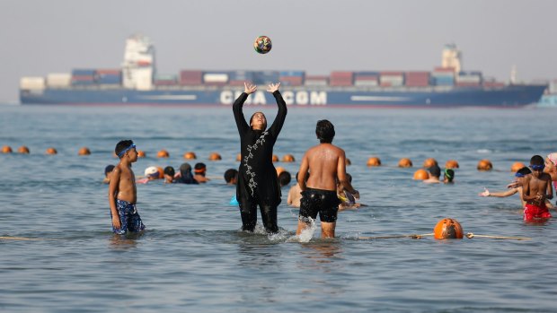 Holidaymakers play as a cargo container ship crosses the Gulf of Suez towards the Red Sea, at El Sokhna beach in Suez, Egypt.