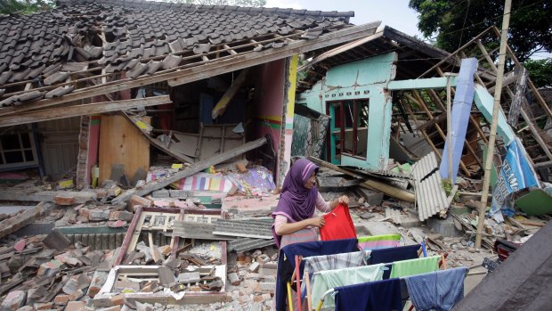 A woman dries her laundry in front of her home destroyed in an earthquake earlier this month. 