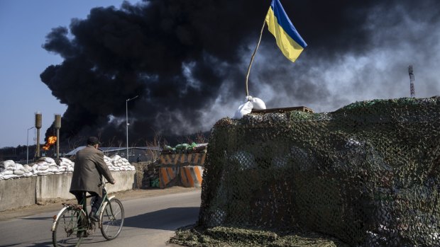 A man rides a bicycle as black smoke rises from a fuel storage of the Ukrainian army following a Russian attack, on the outskirts of Kyiv. 