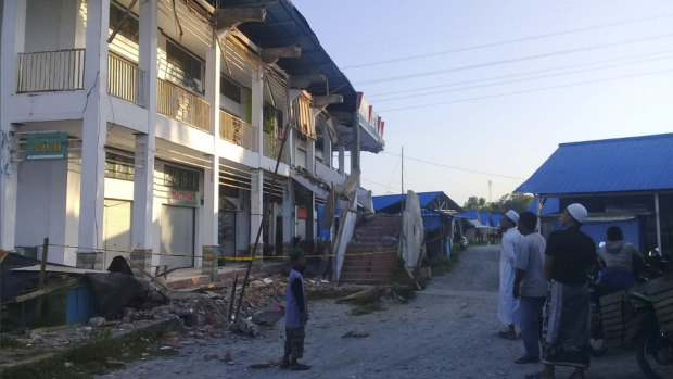People survey a building partially damaged by earthquake in Poso, Central Sulawesi.