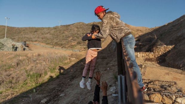 A migrant from Honduras pass a child to her father after he jumped the border fence to get into the US side to San Diego, California this month.
