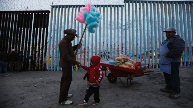 A Honduran migrant boy tries to buy cotton candy from a vendor, but doesn't have enough money, as migrants visit the US border wall to look for opportunities to cross at the beach in Tijuana, Mexico.