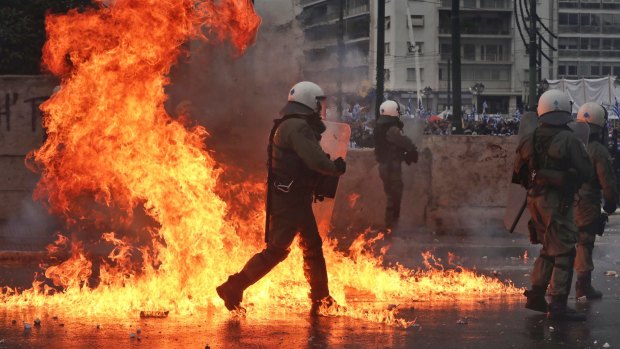 A molotov cocktail explodes next to Greek riot police during clashes after a rally in Athens on Sunday.