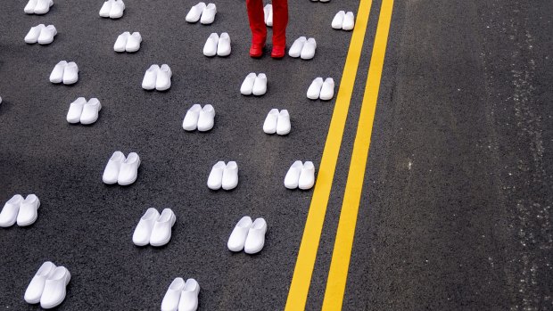 A woman in a nurses uniform stands surrounded by white pairs of shoes to represent the 402 nurses who died because of covid-19, near the White House in Washington.