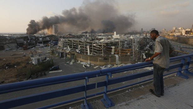 A man surveys destroyed buildings as smoke rises over Beirut.