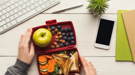 Healthy snack at office workplace. Businesswoman eating organic vegan meals from take away lunch box at wooden working table with computer keyboard and smartphone with empty screen for copy space Desk salad, lunch at work
iStock