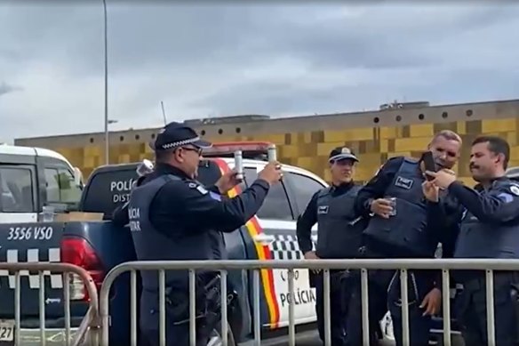 A group of capital police officers films the crowd approaching on their phones in Brasilia on Sunday, January 8 (Monday AEDT)