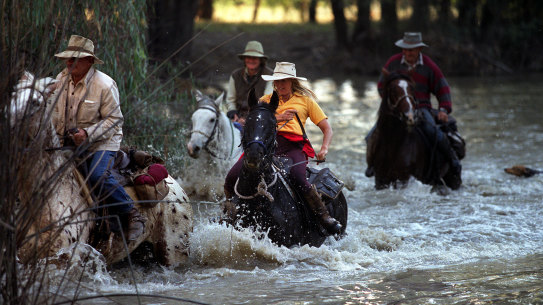 Horse riders cross a river during a muster.