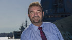 Chief Executive of the Naval Shipbuilding College,  Ian Irving, stands in front of HMAS Hobart during a visit to Garden Island.