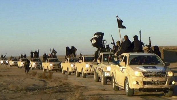 In this undated file photo released online in the summer of 2014 on a militant social media account,  militants of the Islamic State group hold up their weapons and wave its flags on their vehicles in a convoy on a road leading to Iraq, in Raqqa, Syria. 
