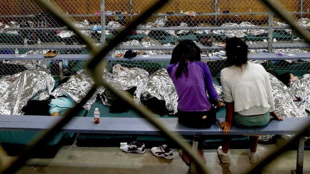 Two girls watch television as others around them sleep in holding cells where hundreds of mostly Central American immigrant children wait to be processed at the US Border Protection Placement Centre in Nogales, Arizona, in 2014.