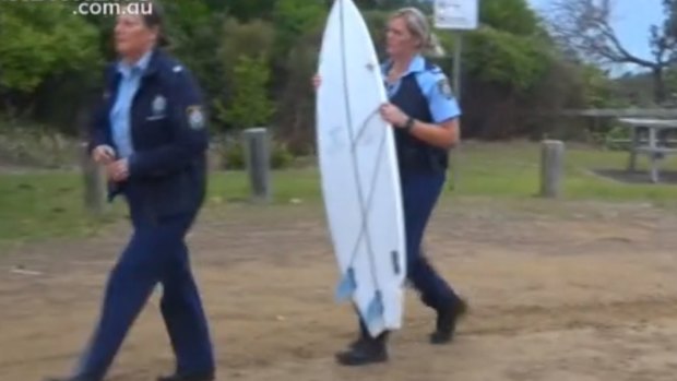 A police officer carries the boy's surfboard at Wooli Beach on Saturday.