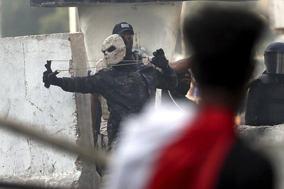 A masked policeman uses a slingshot to fire a stone at demonstrators.
