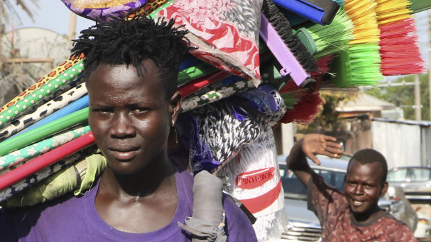 A young merchant carrying brooms to sell walks along a street after the recent ousting of Sudan's President Omar al-Bashir, in the capital Juba, South Sudan. 