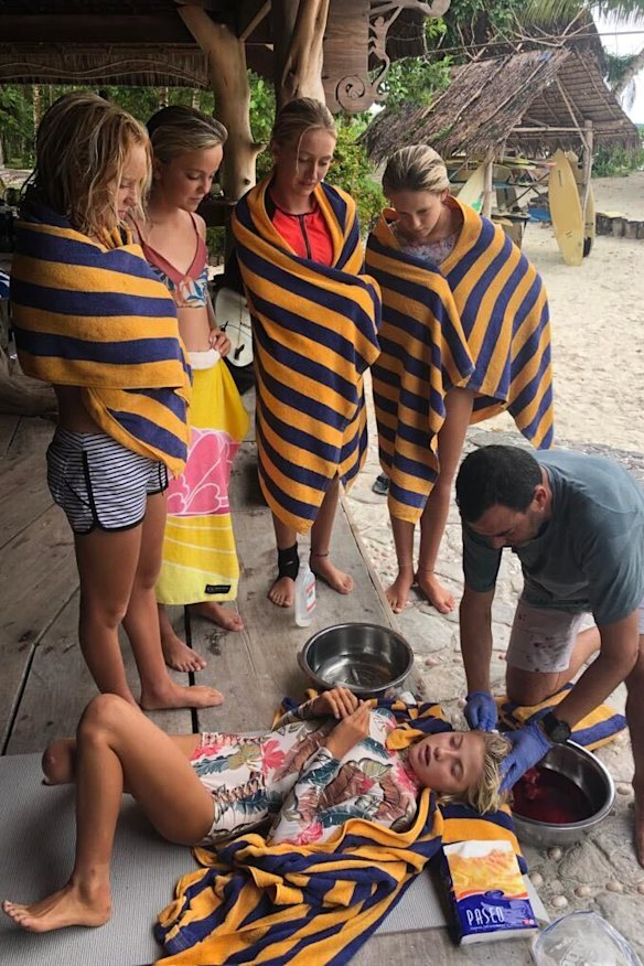 Brooks is stitched up by Dr. Dave Bassler while fellow pro surfers Caity Simmers, Bella Kenworthy, Sierra Kerr and Bela Nalu watch on.