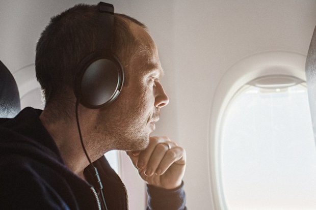 Traveling man on airplane flying charter.  Using smartphone and using noise-cancelling headphones
