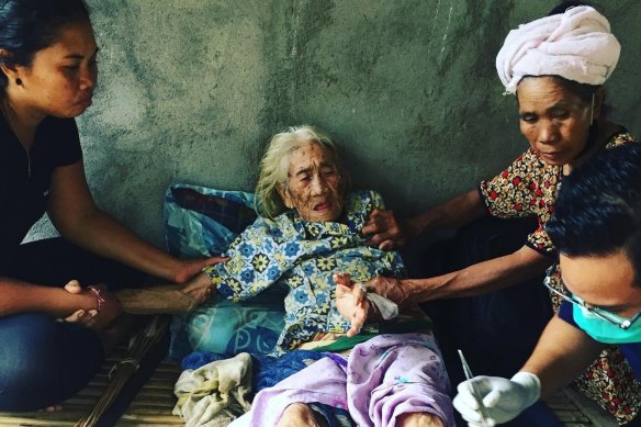 Yayasan Team Action Amed volunteers deliver aid and food packages to an elderly woman.