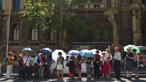 Tourists shield themselves from the sun as they wait for a tram on La Trobe Street.