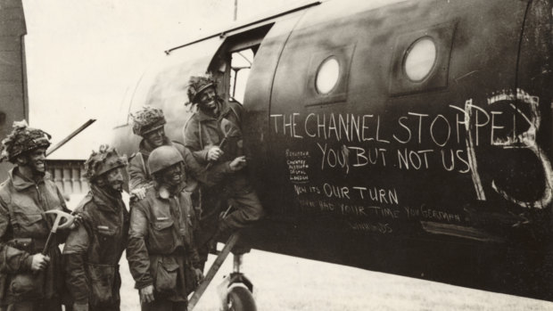 Paratroopers in their war paint reading slogans chalked on a glider.
